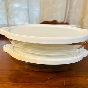 May include: Two white glass bowls with lids. The bowls are stacked on top of each other. The lids are white plastic.