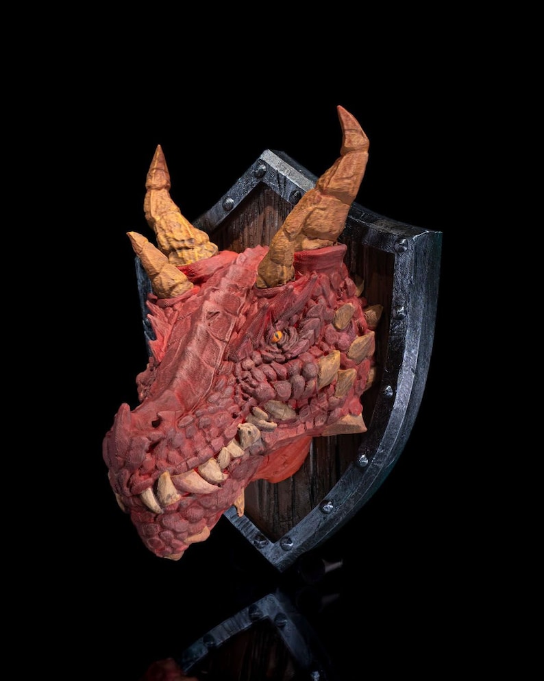 Puede incluir: Una cabeza de drag&oacute;n roja montada en un escudo con un fondo de madera. El drag&oacute;n tiene cuernos y dientes amarillos, y sus ojos est&aacute;n abiertos.