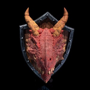 Puede incluir: Una cabeza de drag&oacute;n roja montada en un escudo de madera con un borde de metal negro. El drag&oacute;n tiene cuernos amarillos y dientes afilados.