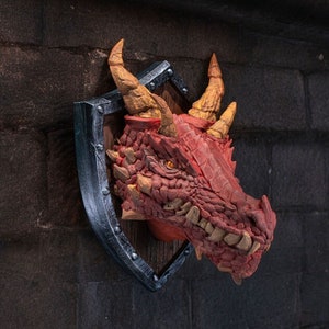 Puede incluir: Una cabeza de drag&oacute;n roja montada en un escudo de madera con un borde de metal plateado. El drag&oacute;n tiene una piel texturizada, escamosa y dientes afilados.