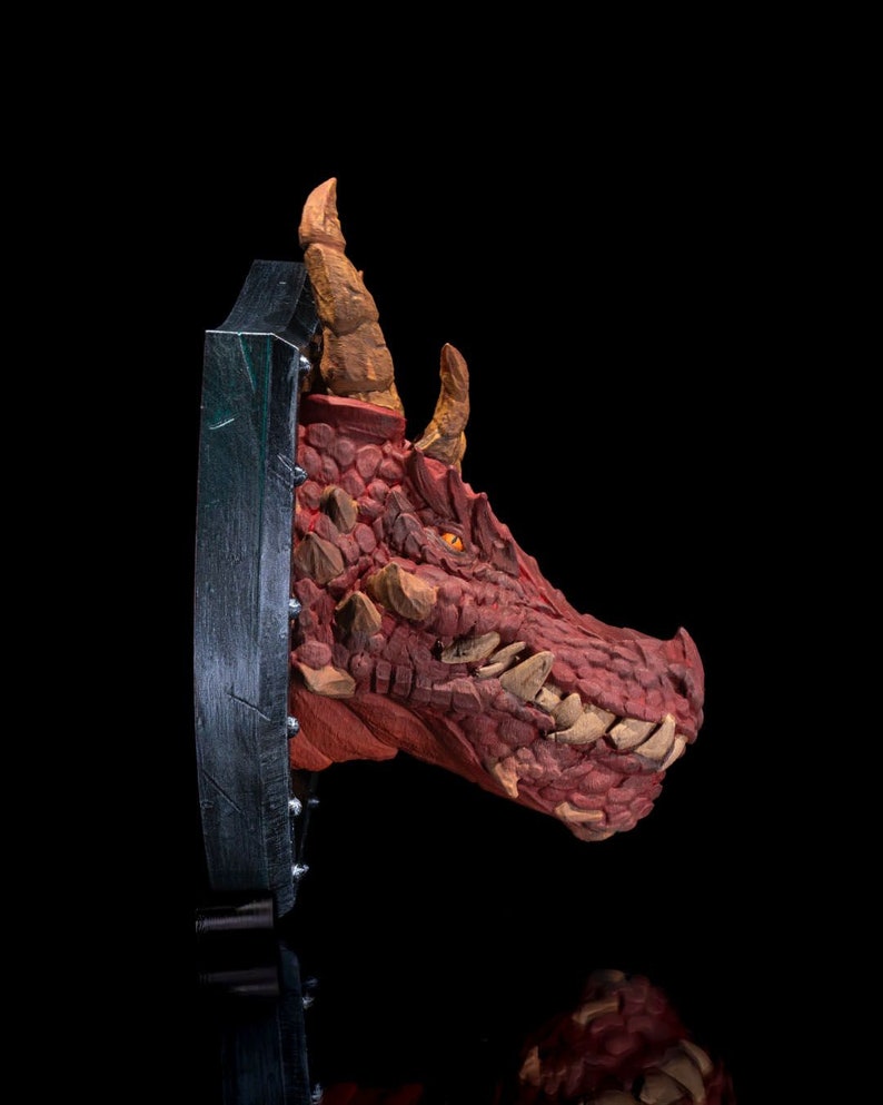 Puede incluir: Una escultura de cabeza de drag&oacute;n roja montada sobre una base circular negra y plateada. El drag&oacute;n tiene una expresi&oacute;n feroz con dientes afilados y una piel texturizada y escamosa.