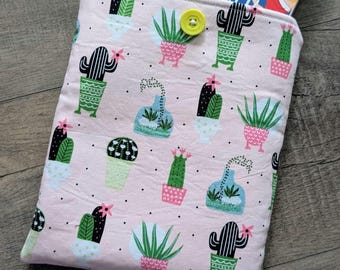 May include: A pink fabric book sleeve featuring a pattern of various cacti in pots. The sleeve has a yellow button closure and holds a book titled "It Happened One Summer."