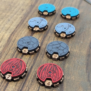 Op de afbeelding: Acht houten spelstukken met verschillende ontwerpen en nummers. De stukken zijn blauw, grijs en rood met zwarte accenten. De nummers op de stukken variëren van 1 tot 7.