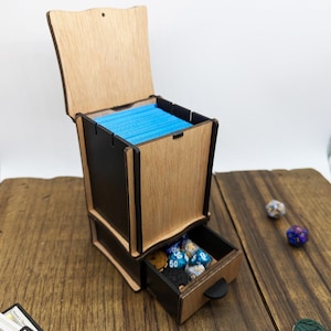 May include: A wooden box with a drawer for storing dice and cards. The box is made of light wood with a dark stain. The drawer is open and contains a variety of dice. The box is sitting on a wooden table.