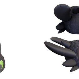 May include: Three black dragon-themed objects are displayed against a white background. The objects include a dragon head with green eyes, a dragon head with large ears, and a dragon wing. The objects are likely toys or collectibles.