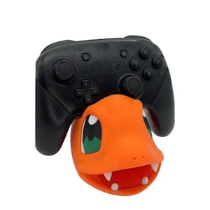 May include: A black Nintendo Switch controller stand shaped like a cartoon orange and red Pokemon character with green eyes.