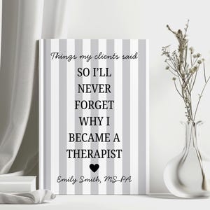 May include: A framed print with a grey and white striped design. The text reads "Things my clients said, SO I'LL NEVER FORGET WHY I BECAME A THERAPIST" with a heart symbol and the name "Emily Smith, MS-PA". A vase with dried flowers is to the right.