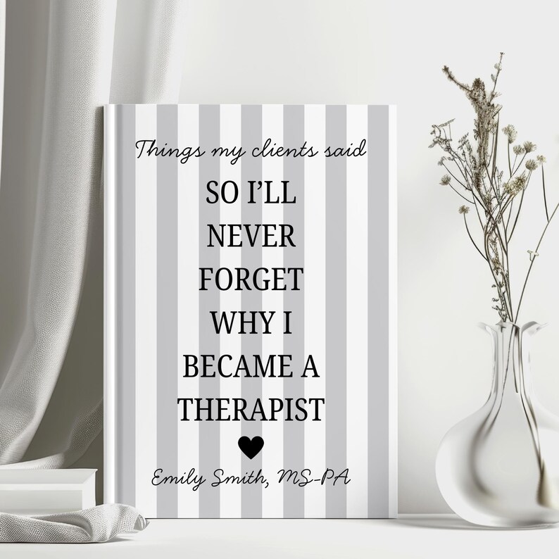 May include: A framed print with a grey and white striped design. The text reads "Things my clients said, SO I'LL NEVER FORGET WHY I BECAME A THERAPIST" with a heart symbol and the name "Emily Smith, MS-PA". A vase with dried flowers is to the right.