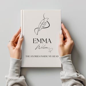 May include: A white hardcover book with the title "EMMA Wilson" and the text "THE STORIES INSIDE MY HEAD" in black. A black line drawing of a feather is above the title. The book is held by two hands.