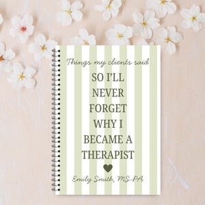 May include: A notebook with a spiral binding, featuring a cover with green and white vertical stripes. The cover displays the text: "Things my clients said, so I'll never forget why I became a therapist." The author's name is also included.