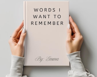 May include: A hardcover book with the title "WORDS I WANT TO REMEMBER" in black text. The author's name, "By: Emma," is written in cursive at the bottom. The book is held by two hands against a light gray background.