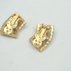 May include: A pair of gold tone clip-on earrings with a geometric design. The earrings are made of metal and have a shiny finish.