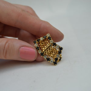 May include: A gold-tone ring with a geometric design featuring black and clear rhinestones.