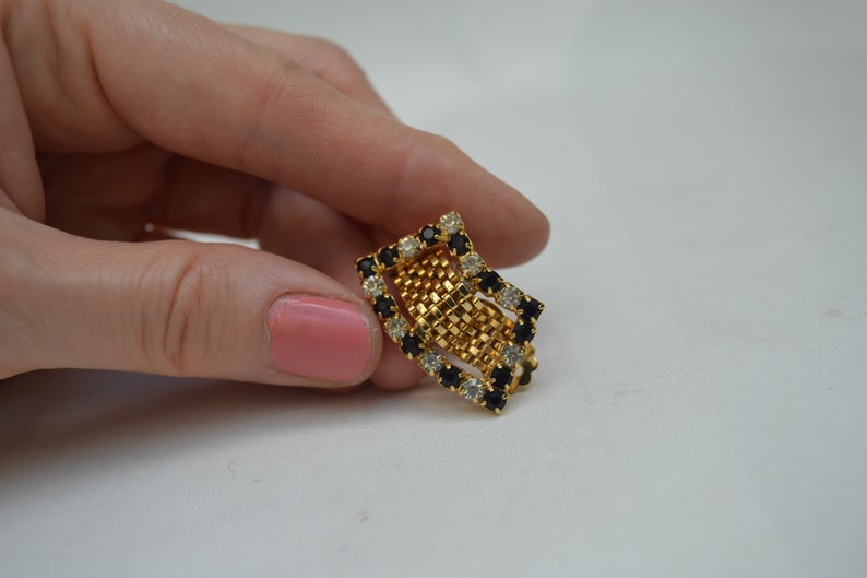 May include: A gold-tone ring with a geometric design featuring black and clear rhinestones.