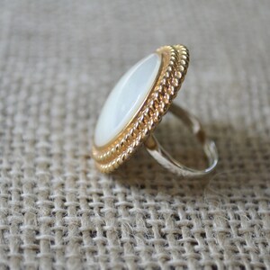 May include: A gold ring with a white oval-shaped stone set in a rope-like design.