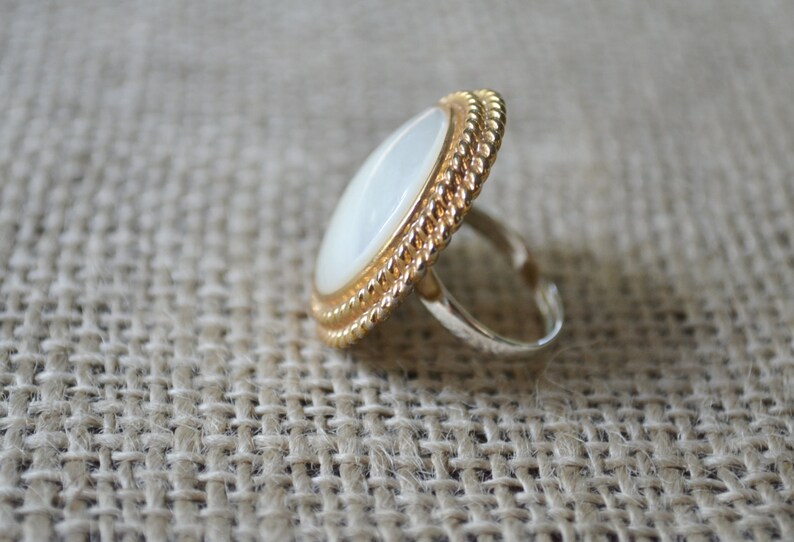May include: A gold ring with a white oval-shaped stone set in a rope-like design.