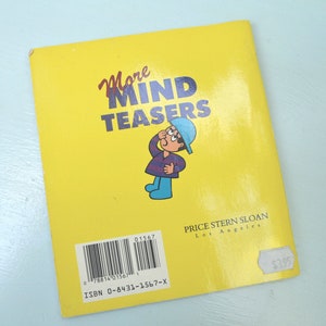 May include: A yellow paperback book titled "More Mind Teasers" with a cartoon illustration of a person wearing a blue hat and a purple and blue striped shirt. The book is published by Price Stern Sloan in Los Angeles. The ISBN is 0-8431-1567-X and the price is $3.95.