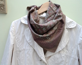 May include: A brown patterned silk scarf with a geometric design. The scarf is folded and draped over a white jacket.
