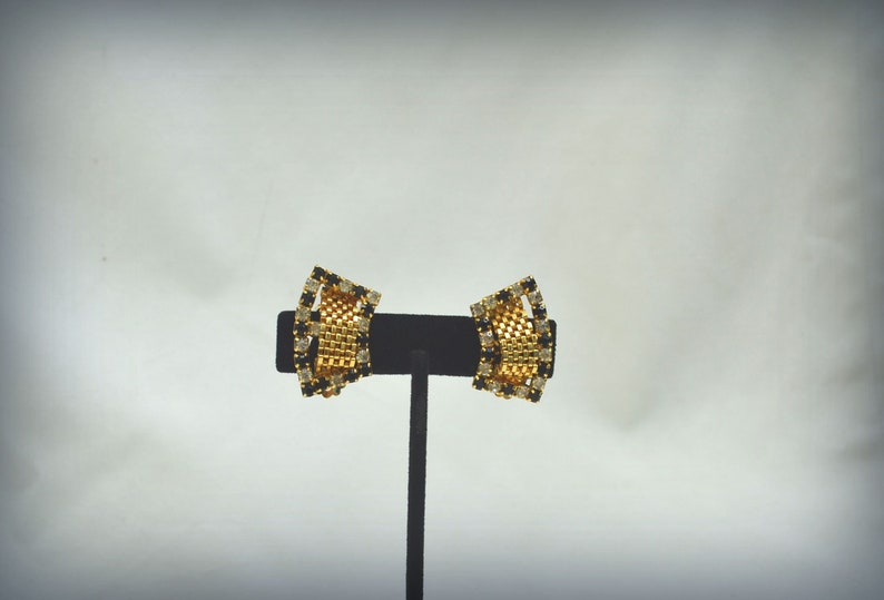 May include: A pair of gold tone clip-on earrings with black and clear rhinestones.