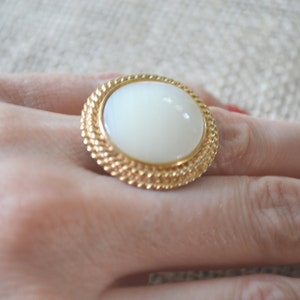 May include: A gold ring with a large white oval cabochon stone set in a rope-like design.