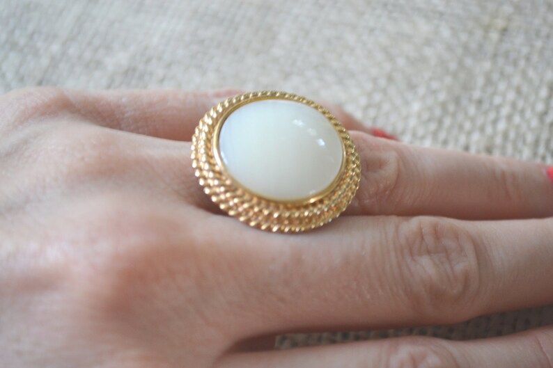 May include: A gold ring with a large white oval cabochon stone set in a rope-like design.