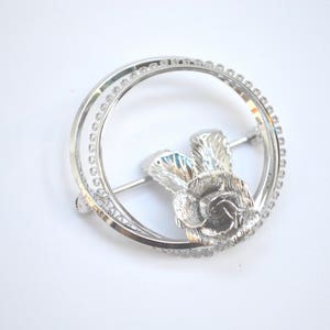 May include: Silver-toned brooch featuring a stylized thistle flower design with a circular frame of small beads.