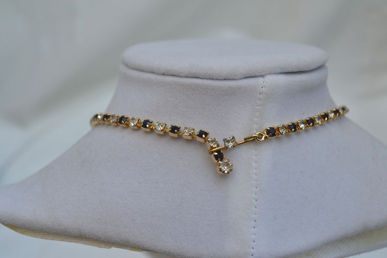 May include: A gold necklace with a chain of alternating black and clear rhinestones. The necklace has a simple clasp.