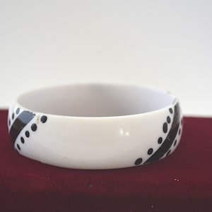 Op de afbeelding: Witte plastic armband met een zwart-wit geometrisch ontwerp.
