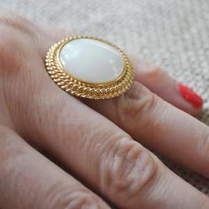 May include: A gold ring with a large white oval-shaped stone set in a textured gold band.