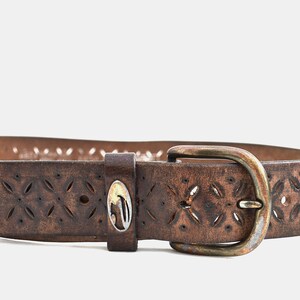 May include: A brown leather belt with a cut-out floral design and a silver oval buckle.