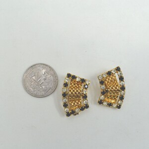 May include: A pair of gold tone clip-on earrings with black and clear rhinestones. The earrings are shaped like a curved rectangle.