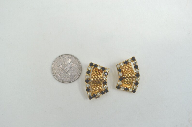 May include: A pair of gold tone clip-on earrings with black and clear rhinestones. The earrings are shaped like a curved rectangle.