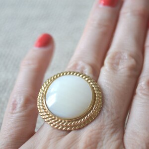 May include: A gold ring with a large white oval-shaped stone set in a rope-like design.