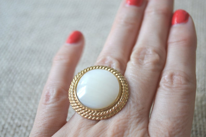 May include: A gold ring with a large white oval-shaped stone set in a rope-like design.