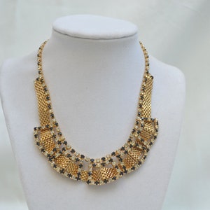 May include: A gold tone necklace with a geometric design featuring black and clear rhinestones.