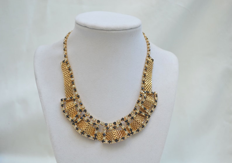 May include: A gold tone necklace with a geometric design featuring black and clear rhinestones.
