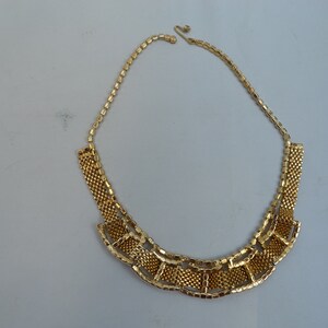 May include: A gold-tone chain necklace with a geometric design. The necklace is made of small, linked squares that form a fan-shaped pattern.