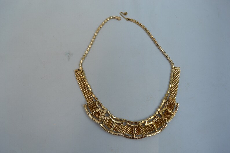 May include: A gold-tone chain necklace with a geometric design. The necklace is made of small, linked squares that form a fan-shaped pattern.