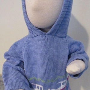 Può includere: Un maglione blu chiaro con cappuccio con un ricamo di barche e boe in bianco, rosa e verde.