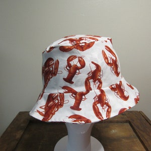 May include: White bucket hat with a brown lobster print.