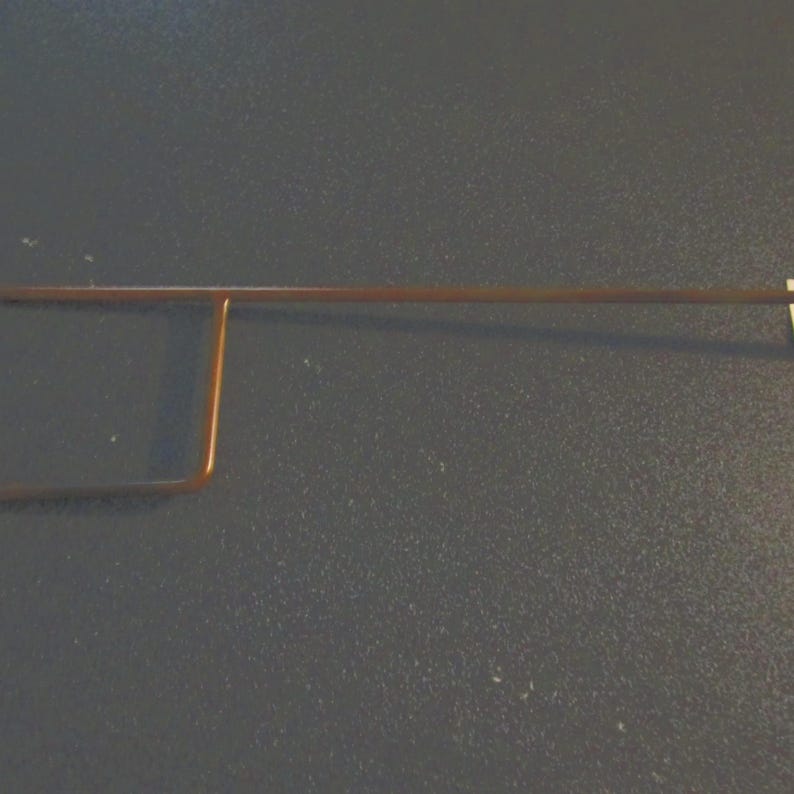 Pu&ograve; includere: Un oggetto metallico color rame con una forma rettangolare e una lunga barra dritta che si estende da esso. L'oggetto &egrave; posto su uno sfondo grigio scuro. Il design sembra essere uno strumento o un componente.