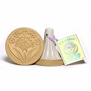 Può includere: Un timbro per biscotti in ceramica con un design floreale. Il timbro è beige con un design floreale marrone. Il timbro è etichettato "CLASSIC COOKIE STAMP".