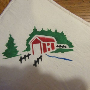 Op de afbeelding: Een witte doek met een handgeschilderd ontwerp met een rode overdekte brug, groene bomen, een blauwe beek en een zwart hek. Het ontwerp is gecentreerd op de doek.