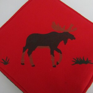 Op de afbeelding: Rode stoffen onderzetter met een zwart silhouet van een eland en groen gras.