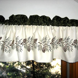 May include: Cream-colored valance with a repeating pattern of brown pinecones and branches. The top edge features a dark green, ruffled fabric. The valance is hanging above a window, adding a touch of nature-inspired decor to the room.