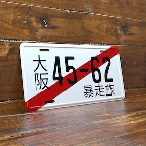 May include: White license plate with a red diagonal stripe. The plate features black Japanese characters and the numbers "45-62". The Japanese characters read "Osaka" and "bosozoku".