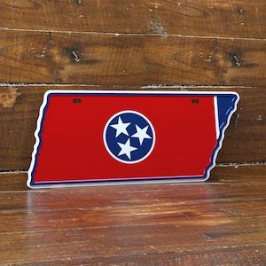 Könnte beinhalten: Ein Kennzeichen in Form des Bundesstaates Tennessee. Es hat einen roten Hintergrund mit einem weißen Kreis mit drei weißen Sternen. Der Rand ist blau und weiß.