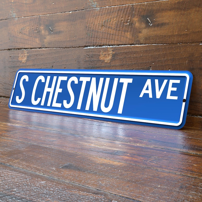 May include: A blue street sign with white lettering that reads "S CHESTNUT AVE". The sign has a white border and is mounted on a wooden surface. The sign is angled slightly, showing the text in a clear, readable font.