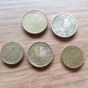 May include: Five gold-coloured Spanish euro coins featuring the image of Miguel de Cervantes and the text "ESPAÑA" on each coin. The coins are dated 1999, 2000, 2001, and 2005.