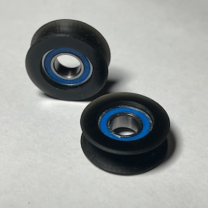 May include: Two black plastic pulleys with blue bearing rings. The pulleys are used for string or rope.
